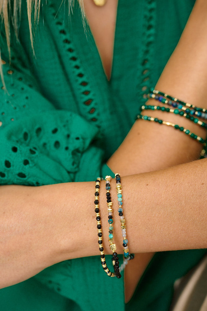 A lifestyle shot showcasing the Amaryllis triple-wrap stretch bracelet elegantly worn amongst stacking malachite bracelets with an elegant green shirt.