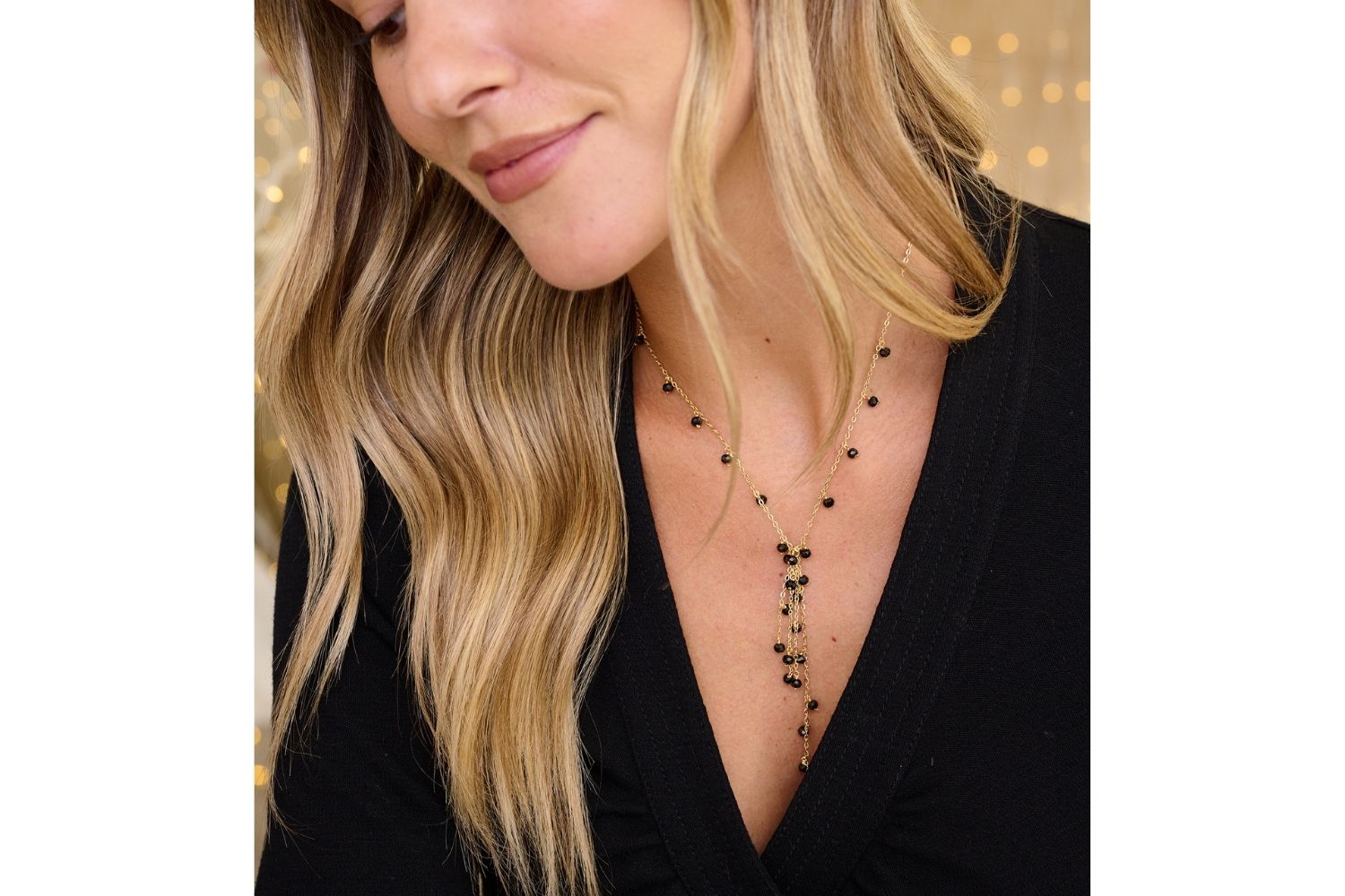 Ivy Black Spinel Gemstone Lariat Necklace styled with a V neck neckline, featuring sleek black spinel gemstones and warm gold tones, ideal day to night piece